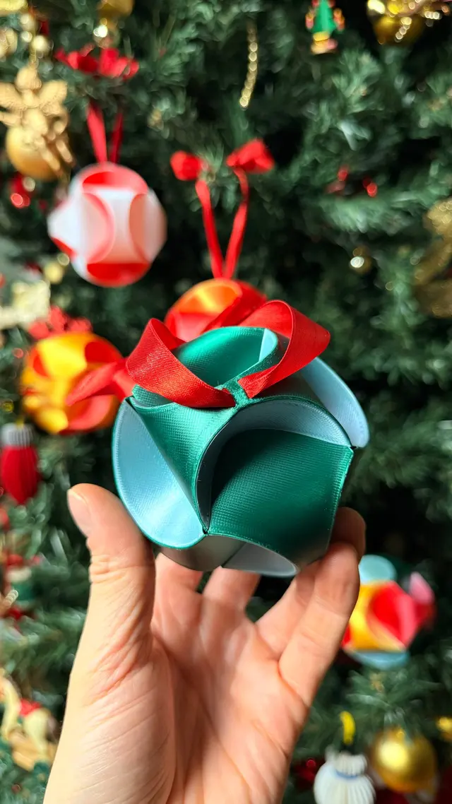 Una mano tiene la Fold Star multicolore davanti all'albero di Natale