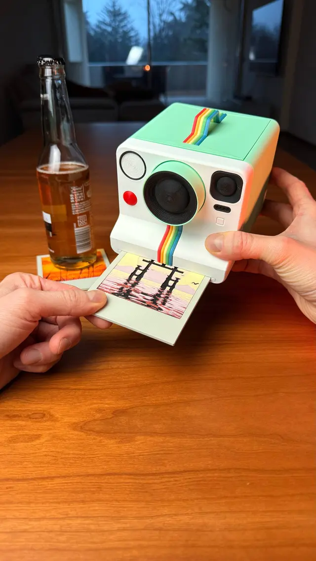 Una mano preme il pulsante e un sottobicchiere esce dalla fotocamera