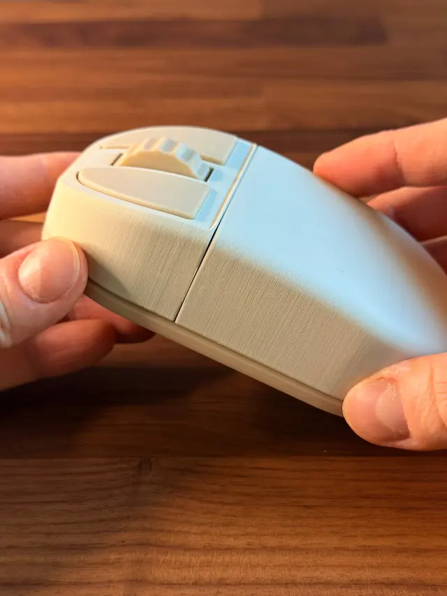 Apribottiglie a forma di mouse beige tenuto tra le mani, visto di lato, con due tasti e rotella