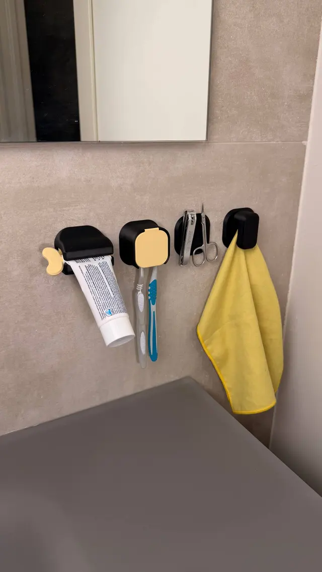 Gli organizer Tidy Wall neri fissati alla parete del bagno, con dentifricio, spazzolini e asciugamano